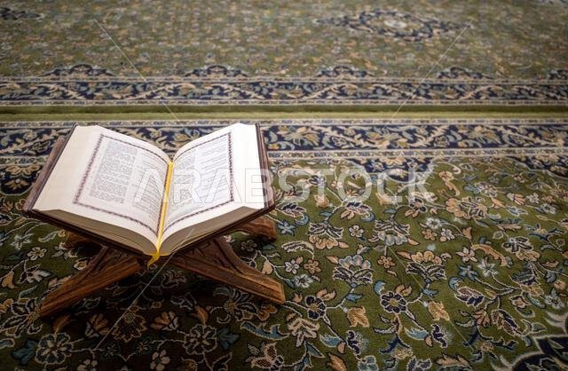 كتاب مقدس مفتوح من القرآن الكريم موضوع على سجادة خضراء في المسجد النبوي في مدينة المدينة المنورة بالمملكة العربية السعودية.