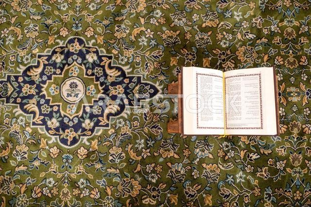 كتاب مقدس مفتوح من القرآن الكريم موضوع على سجادة خضراء في المسجد النبوي في مدينة المدينة المنورة بالمملكة العربية السعودية.