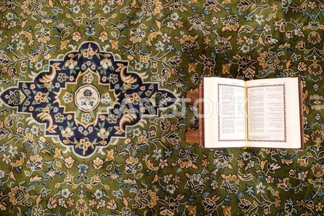 كتاب مقدس مفتوح من القرآن الكريم موضوع على سجادة خضراء في المسجد النبوي في مدينة المدينة المنورة بالمملكة العربية السعودية.