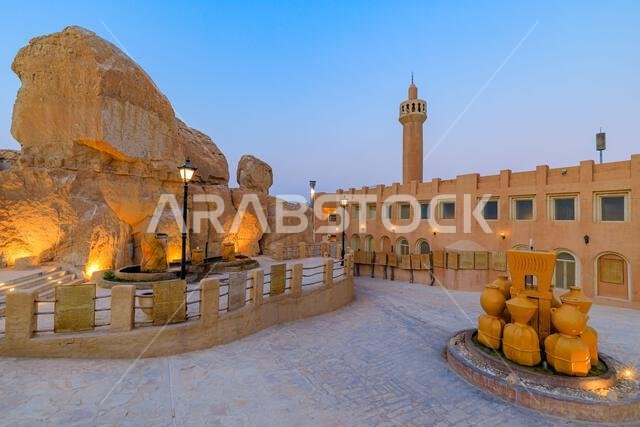 كهوف صخرية مضاءة ومسجد جبل القره مع نافورة عند الغسق في واحة الأحساء، المملكة العربية السعودية، تُظهر الثقافة والتراث المحليين كهوف صخرية مضاءة ومسجد جبل القره مع نافورة عند الغسق في واحة الأحساء، المملكة العربية السعودية، تُظهر الثقافة والتراث المحليين