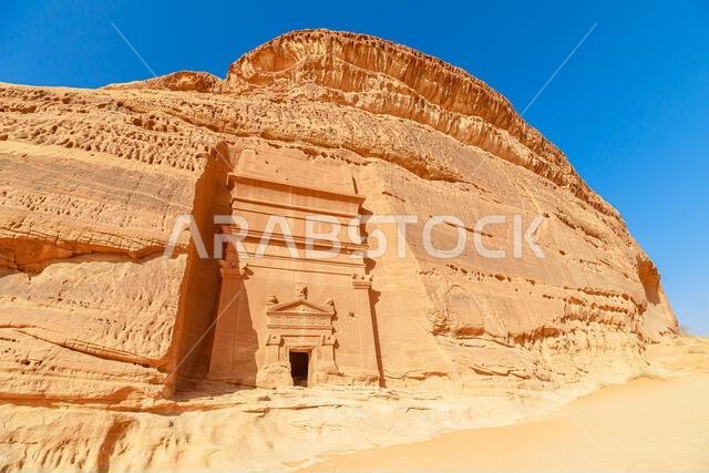 Sunlight illuminating the intricate facade of a Nabataean tomb carved into sandstone cliffs of Jabal AlBanat at the ancient city of Hegra, a UNESCO Sunlight illuminating the intricate facade of a Nabataean tomb carved into sandstone cliffs of Jabal AlBanat at the ancient city of Hegra, a UNESCO