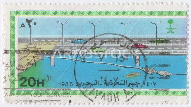 المملكة العربية السعودية - 26 نوفمبر 1986: طابع بريدي متعدد الألوان بقيمة 20 هلالة يصور جسر الطريق السريع بين البحرين والمملكة العربية السعودية. افتتاح الطريق السريع السعودي البحريني. جسر الملك فهد عبارة عن سلسلة من الجسور والطرق السريعة بطول 25 كيلومترًا تربط بين مدينة الخبر في المملكة العربية السعودية ومدينة الجسرة في البحرين. تم تحويل أحد الجسور، المعروف باسم الجزيرة الوسطى، إلى جزيرة اصطناعية كبيرة تضم مرافق جمركية وهجرة، ومسجدًا وحدائق ومطاعم للوجبات السريعة. جزيرة أخرى