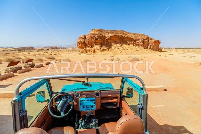 Turquoise SUV beside ancient rock-cut tombs Jabal Al-Ahmar at the Hegra archaeological site in Al-Ula, blending modern tourism with historical