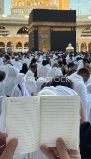 A pilgrim holds a small notebook with a heart doodle in front of the Kaaba in Mecca, Saudi Arabia. The sacred site is surrounded by worshippers