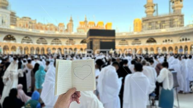 A pilgrim holds a small notebook with a heart doodle in front of the Kaaba in Mecca, Saudi Arabia. The sacred site is surrounded by worshippers