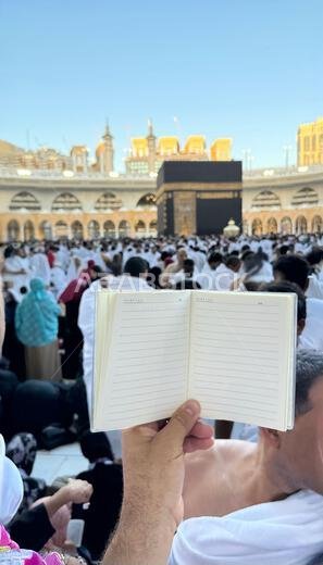 A pilgrim holds a small notebook with a heart doodle in front of the Kaaba in Mecca, Saudi Arabia. The sacred site is surrounded by worshippers