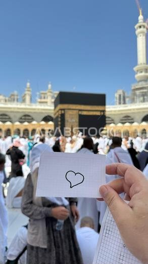 A pilgrim holds a small notebook with a heart doodle in front of the Kaaba in Mecca, Saudi Arabia. The sacred site is surrounded by worshippers A pilgrim holds a small notebook with a heart doodle in front of the Kaaba in Mecca, Saudi Arabia. The sacred site is surrounded by worshippers