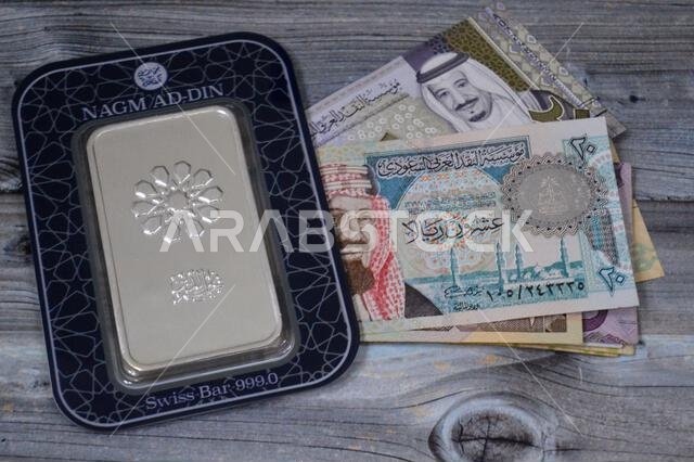 Cairo, Egypt, February 20 2025: Saudi riyals money banknotes and Nagm Ad-Din pure fine silver 250 grams bar, silver investment, exchange price rate, i