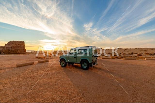 Stunning sunset illuminating a safari 4x4 car parked beside the majestic Qasr Al Farid, an ancient Nabataean tomb in the Hegra desert, Al Ula, Saudi