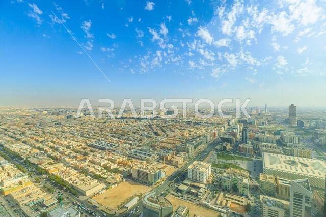 منظر بانورامي للرياض، عاصمة المملكة العربية السعودية، يُظهر امتدادها العمراني الشاسع، وهندستها المعمارية الحديثة، وشوارعها الصاخبة تحت سماء صافية.
