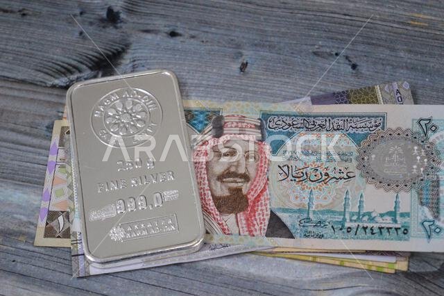 القاهرة، مصر، 20 فبراير 2025: أوراق نقدية من الريال السعودي وسبائك فضة نقية من تصميم نجم الدين بوزن 250 غرامًا، استثمار في الفضة، سعر الصرف، i