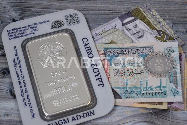 Cairo, Egypt, February 20 2025: Saudi riyals money banknotes and Nagm Ad-Din pure fine silver 250 grams bar, silver investment, exchange price rate, i