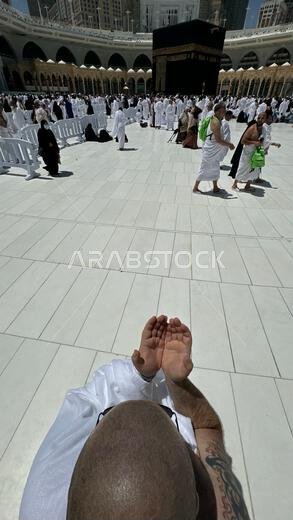 رجل أصلع يقف لالتقاط صورة أمام الكعبة المشرفة ظهرًا بعد أداء العمرة في المسجد الحرام بمكة المكرمة، وهي مناسك الحج الإسلامية المقدسة في قلب العالم.