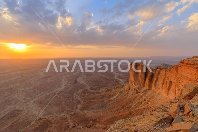 غروب الشمس الذهبي يضيء مشهداً صحراوياً شاسعاً من حافة الجرف العالمي، مسلطاً الضوء على المنحدرات الدرامية لجبل طويق غروب الشمس الذهبي يضيء مشهداً صحراوياً شاسعاً من حافة الجرف العالمي، مسلطاً الضوء على المنحدرات الدرامية لجبل طويق