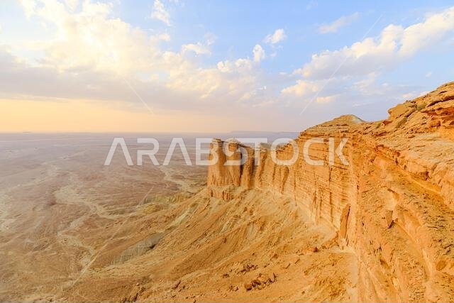 منحدرات جبال طويق الشاهقة عند غروب الشمس تخلق منظراً خلاباً على صحراء مترامية الأطراف بالقرب من الرياض، المملكة العربية السعودية، مما يبرز جمالها