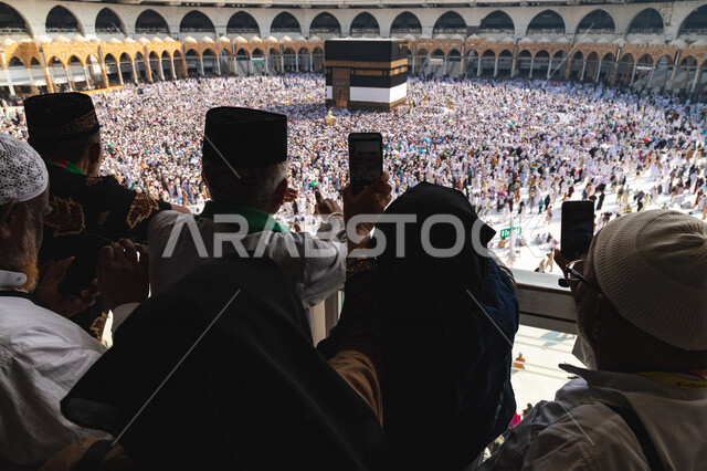 صورة من الخلف لمجموعة من الحجاج يقومون بالتقاط صور للكعبة المشرفة، حجاج يطوفون حول الكعبة، أداء مناسك الحج والعمرة، العبادة والتقرب الى الله، موسم الحج 2022، اسلاميات وعبادة