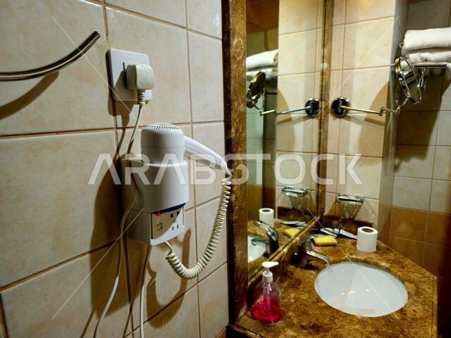 Medina, Saudi Arabia, June 26 2024: a shower cabin stall with a glass barrier, bathroom basin, toilet seat and hair dryer, in a hotel in Madinah city Medina, Saudi Arabia, June 26 2024: a shower cabin stall with a glass barrier, bathroom basin, toilet seat and hair dryer, in a hotel in Madinah city