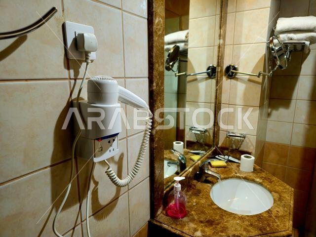Medina, Saudi Arabia, June 26 2024: a shower cabin stall with a glass barrier, bathroom basin, toilet seat and hair dryer, in a hotel in Madinah city