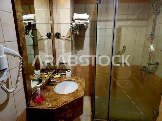 Medina, Saudi Arabia, June 26 2024: a shower cabin stall with a glass barrier, bathroom basin, toilet seat and hair dryer, in a hotel in Madinah city Medina, Saudi Arabia, June 26 2024: a shower cabin stall with a glass barrier, bathroom basin, toilet seat and hair dryer, in a hotel in Madinah city