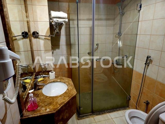 Medina, Saudi Arabia, June 26 2024: a shower cabin stall with a glass barrier, bathroom basin, toilet seat and hair dryer, in a hotel in Madinah city