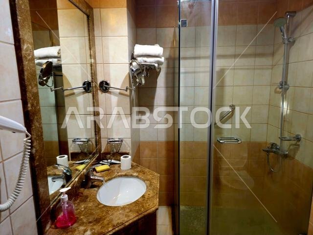 Medina, Saudi Arabia, June 26 2024: a shower cabin stall with a glass barrier, bathroom basin, toilet seat and hair dryer, in a hotel in Madinah city