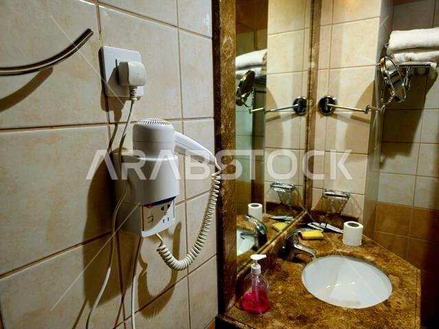 Medina, Saudi Arabia, June 26 2024: a shower cabin stall with a glass barrier, bathroom basin, toilet seat and hair dryer, in a hotel in Madinah city Medina, Saudi Arabia, June 26 2024: a shower cabin stall with a glass barrier, bathroom basin, toilet seat and hair dryer, in a hotel in Madinah city