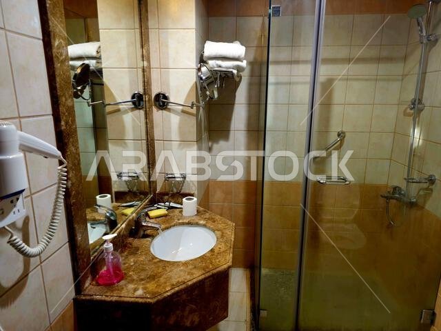 Medina, Saudi Arabia, June 26 2024: a shower cabin stall with a glass barrier, bathroom basin, toilet seat and hair dryer, in a hotel in Madinah city Medina, Saudi Arabia, June 26 2024: a shower cabin stall with a glass barrier, bathroom basin, toilet seat and hair dryer, in a hotel in Madinah city