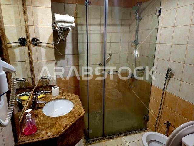 Medina, Saudi Arabia, June 26 2024: a shower cabin stall with a glass barrier, bathroom basin, toilet seat and hair dryer, in a hotel in Madinah city Medina, Saudi Arabia, June 26 2024: a shower cabin stall with a glass barrier, bathroom basin, toilet seat and hair dryer, in a hotel in Madinah city