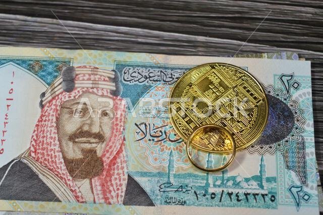 Saudi Arabian money banknotes bills of SAR riyals and Bitcoin physical golden coin, BTC the 1st decentralized cryptocurrency and a gold ring pure yell