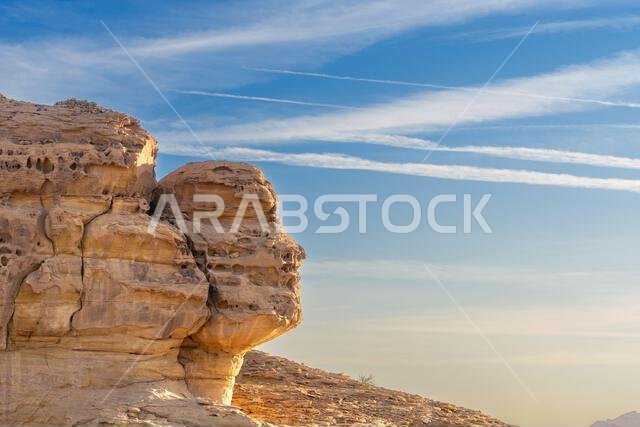 صخرة الوجه عند غروب الشمس، إحدى عجائب الطبيعة قرب صخرة الحجر الرملي المنحوتة في جبل الأحمر، ومقابر الحِجر القديمة في صحراء العلا، المملكة العربية السعودية