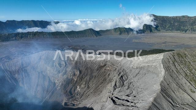 A dramatic bird eye view reveals the immense crater of Mount Bromo, with mist swirling above the rugged volcanic landscape and distant ridges under a