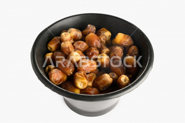 سله سوداء مليئه برطب منيفي من نخيل المملكه العربيه السعوديه, حصاد النخيل في مزارع المملكه, تمر منيفي, رطب نوع فاخر بخلفية بيضاء