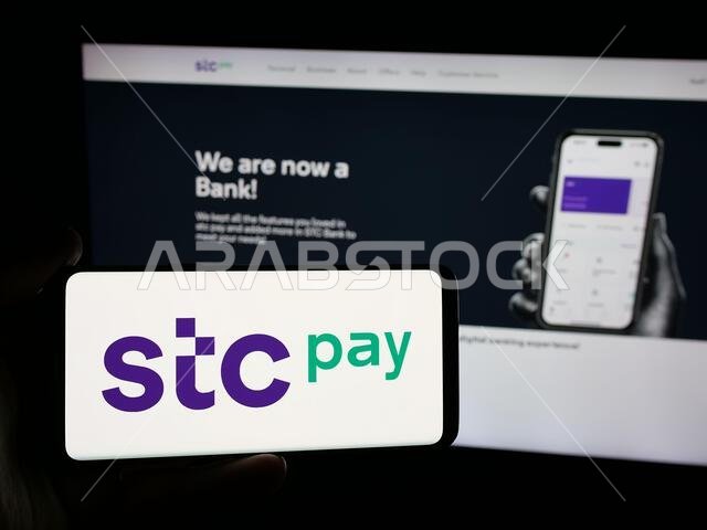 شتوتغارت، ألمانيا - 13-06-2025: شخص يحمل هاتفًا ذكيًا عليه شعار محفظة STC Pay الرقمية الآمنة السعودية على الشاشة أمام الموقع الإلكتروني.