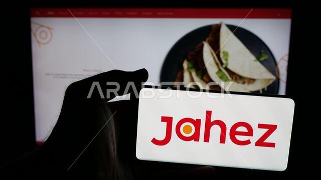 Stuttgart, Germany - 06-13-2025: Person holding mobile phone with logo of Saudi Arabian food delivery app company Jahez on screen in front of web page