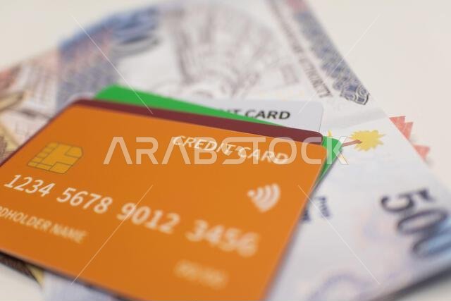 بطاقة ائتمان برتقالية على رزمة من الأوراق النقدية بالريال السعودي.