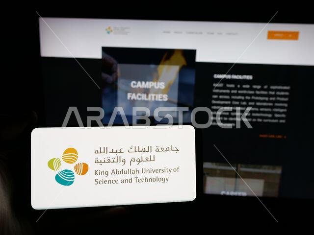 شتوتغارت، ألمانيا - 14-06-2025: شخص يحمل هاتفًا ذكيًا عليه شعار جامعة الملك عبد الله السعودية (كاوست) على الشاشة أمام موقع إلكتروني.
