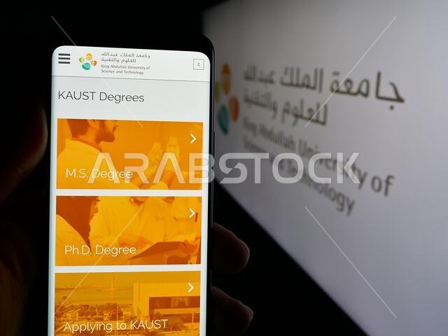 شتوتغارت، ألمانيا - 14-06-2025: شخص يحمل هاتفًا محمولًا يعرض صفحة جامعة الملك عبد الله للعلوم والتقنية (كاوست) أمام شعار الجامعة.