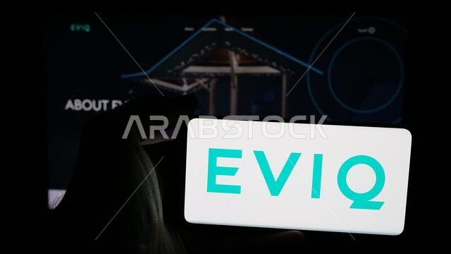 Stuttgart, Germany - 06-14-2025: Person holding mobile phone with logo of Electric Vehicle Infrastructure Company EVIQ on screen in front of web page. Stuttgart, Germany - 06-14-2025: Person holding mobile phone with logo of Electric Vehicle Infrastructure Company EVIQ on screen in front of web page.