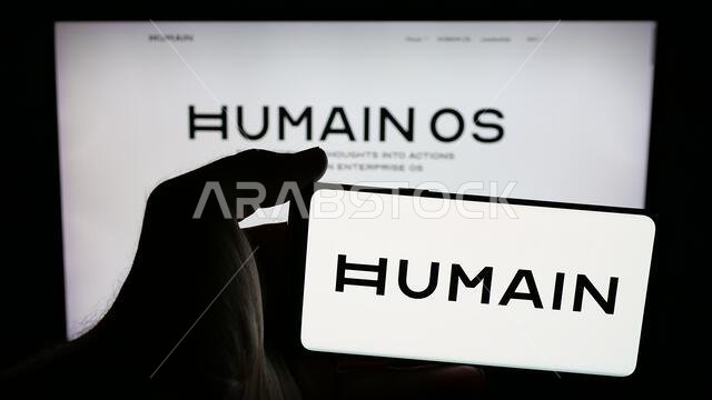 شتوتغارت، ألمانيا - 06-12-2025: شخص يحمل هاتفًا محمولًا عليه شعار شركة الذكاء الاصطناعي السعودية "هيومين" على الشاشة أمام صفحة ويب.
