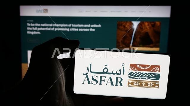 Stuttgart, Germany - 06-14-2025: Person holding mobile phone with logo of Saudi tourism investment company ASFAR on screen in front of web page.