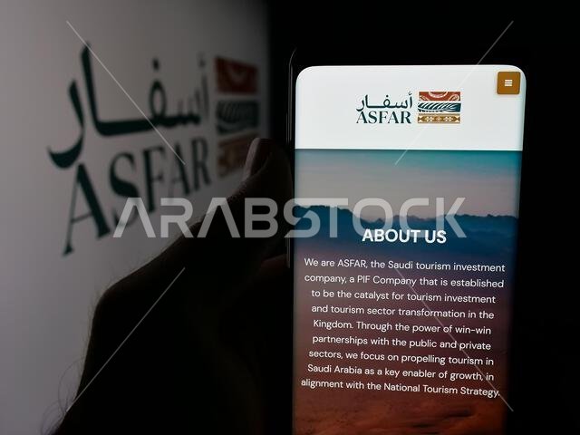Stuttgart, Germany - 06-14-2025: Person holding smartphone with web page of Saudi tourism investment company ASFAR on screen in front of logo.