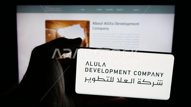 Stuttgart, Germany - 06-13-2025: Person holding mobile phone with logo of business Al-Ula Development Company (UDC) on screen in front of web page.