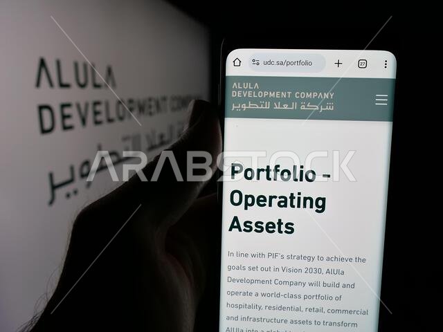 شتوتغارت، ألمانيا - 13-06-2025: شخص يحمل هاتفًا محمولًا يعرض صفحة ويب لشركة العلا للتطوير (UDC) أمام الشعار.