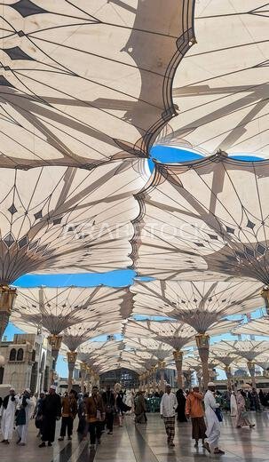 المدينة المنورة، المملكة العربية السعودية - 6 مارس 2024: الحجاج يسيرون إلى المسجد النبوي الشريف تحت مظلة عملاقة استعداداً للصلاة.