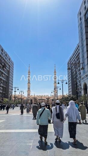Medina, Saudi Arabia - March 6, 2024:  Pilgrims walk to the main mosque of the Prophet Muhammad Al-Masjid an-Nabawi underneath giant umbrella preparin