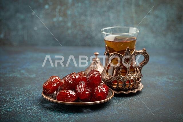 Breaking fasting with dried dates during Ramadan Kareem, Iftar meal with dates and Arab tea in traditional glass, angle view on rustic blue background