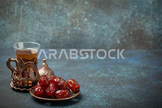 Breaking fasting with dried dates during Ramadan Kareem, Iftar meal with dates and Arab tea in traditional glass, angle view on rustic blue background