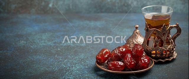 Breaking fasting with dried dates during Ramadan Kareem, Iftar meal with dates and Arab tea in traditional glass, angle view on rustic blue background
