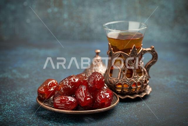 Breaking fasting with dried dates during Ramadan Kareem, Iftar meal with dates and Arab tea in traditional glass, angle view on rustic blue background