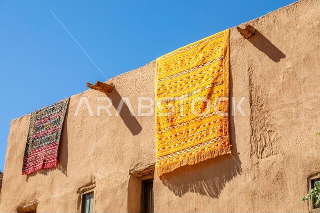 سجاد عربي مزخرف معلق من أسطح المنازل الطينية التقليدية، العلا، منطقة المدينة المنورة، المملكة العربية السعودية سجاد عربي مزخرف معلق من أسطح المنازل الطينية التقليدية، العلا، منطقة المدينة المنورة، المملكة العربية السعودية